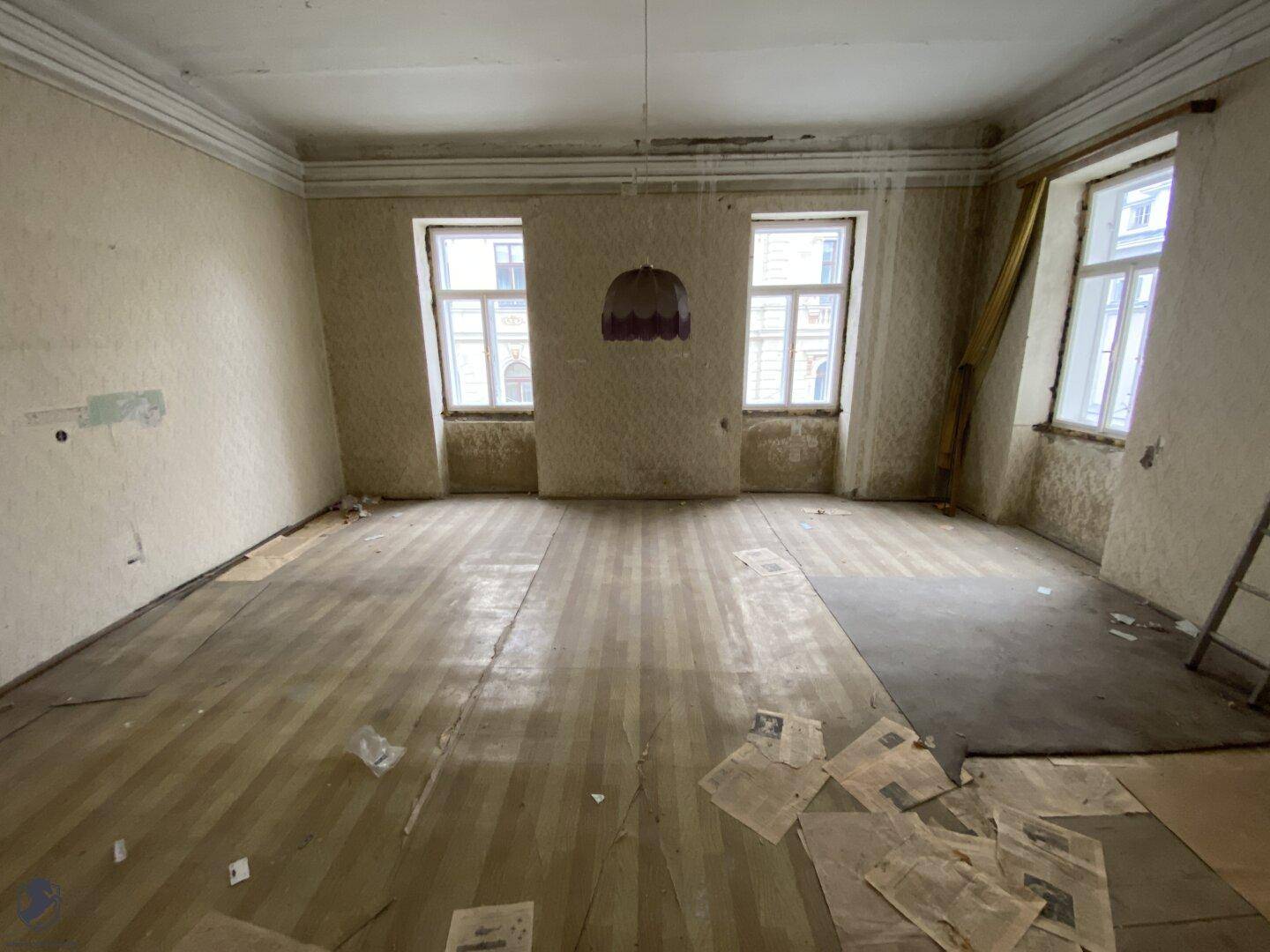 Großer, unrenovierter Raum mit Holzdielenboden und mehreren Fenstern, die viel Tageslicht hereinlassen.