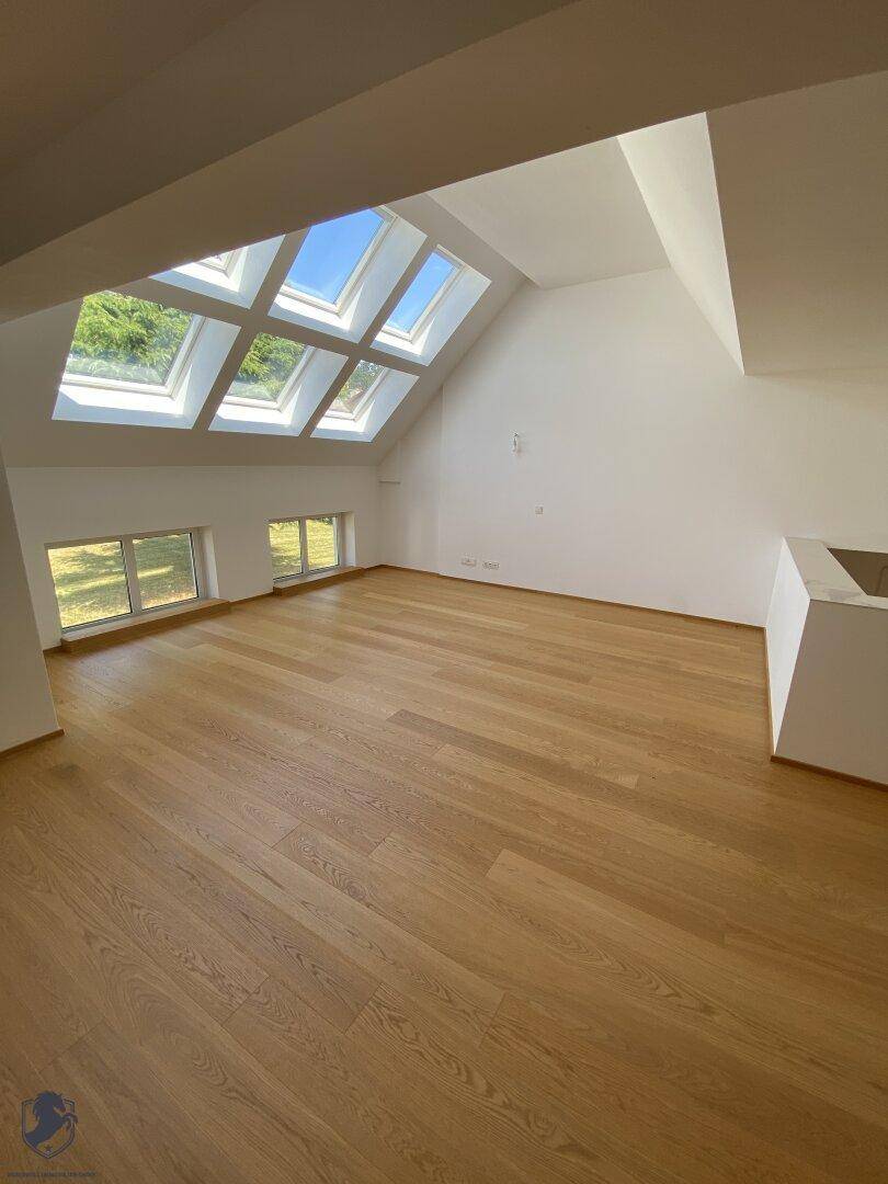 Heller Raum mit Holzdielenboden, weißen Wänden und zahlreichen Dachfenstern für viel Tageslicht.