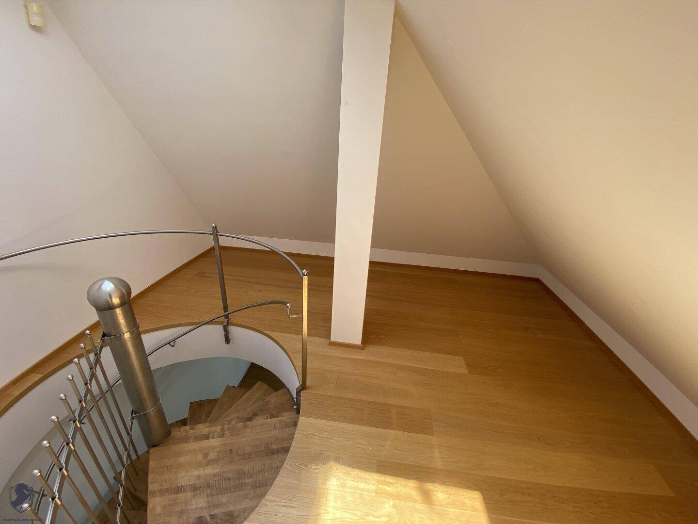 Elegante Wendeltreppe mit Metallgeländer in einem hellen Dachgeschossbereich.
