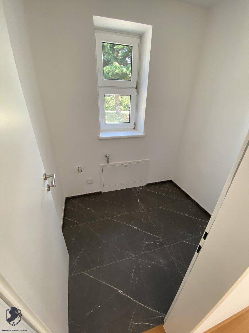 Kleiner Raum mit dunklem Fliesenboden, weißen Wänden und einem Fenster, ideal als Gäste-WC.
