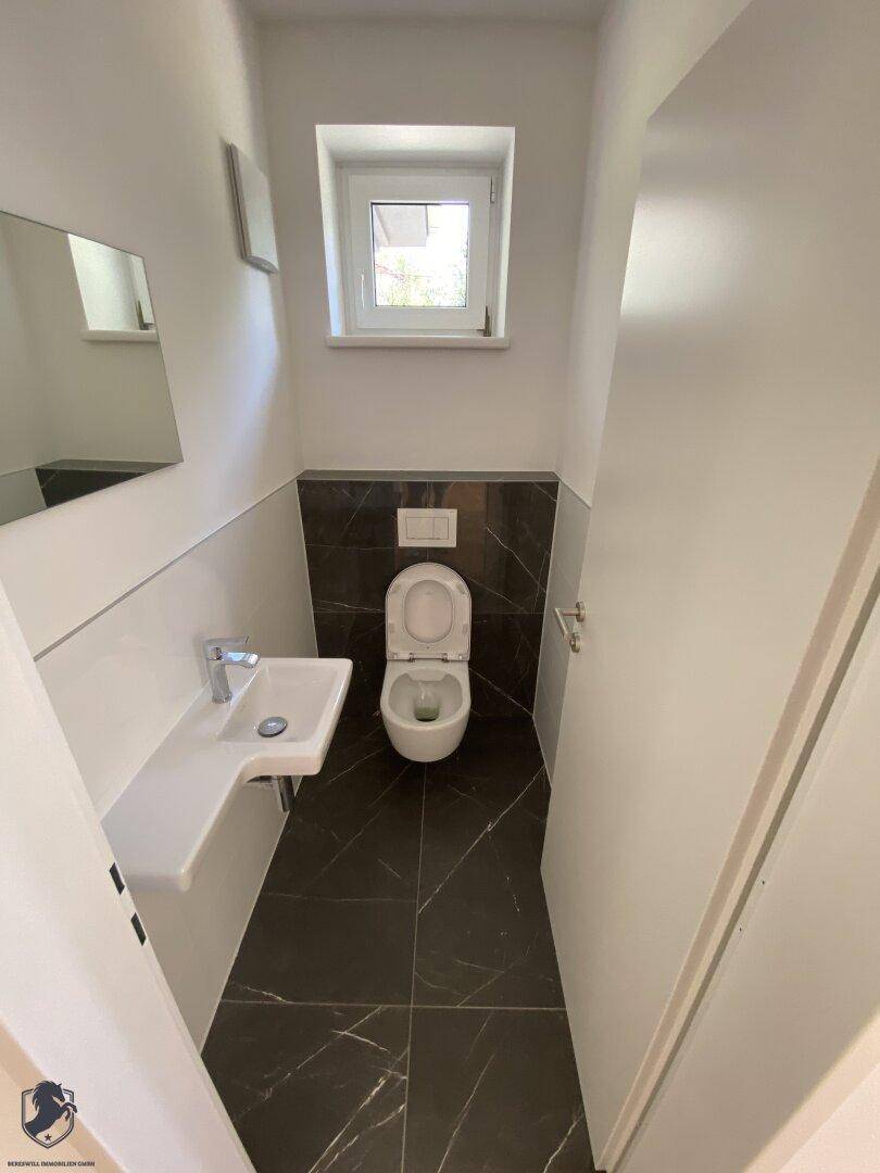 Modernes Gäste-WC mit dunklen Fliesen, kleinem Waschbecken und Fenster.