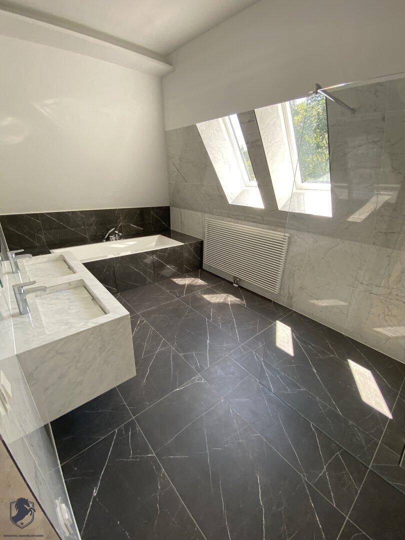 Modernes Badezimmer mit doppelten Marmorwaschbecken, Badewanne und Dachfenstern.
