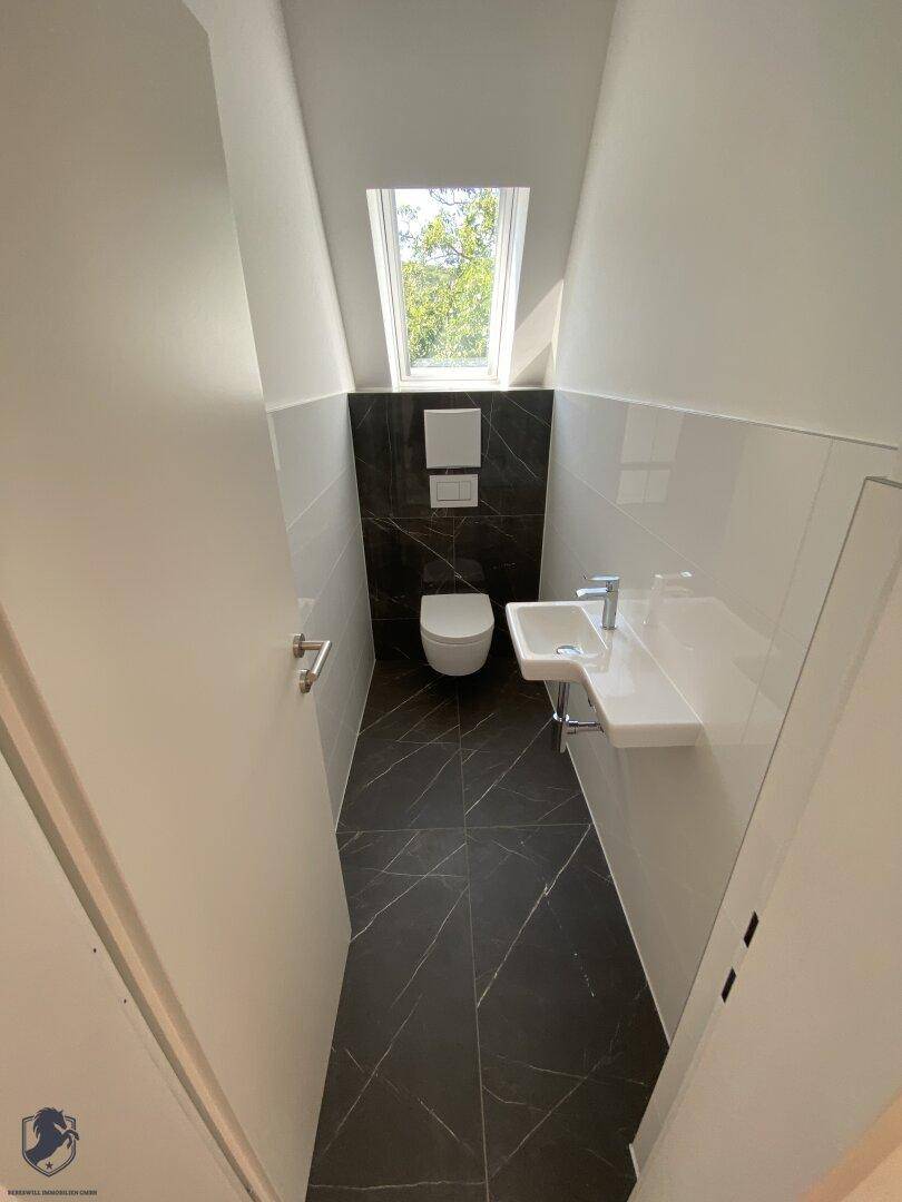 Modernes Gäste-WC mit dunklen Fliesen, wandhängendem WC und kleinem Waschbecken.