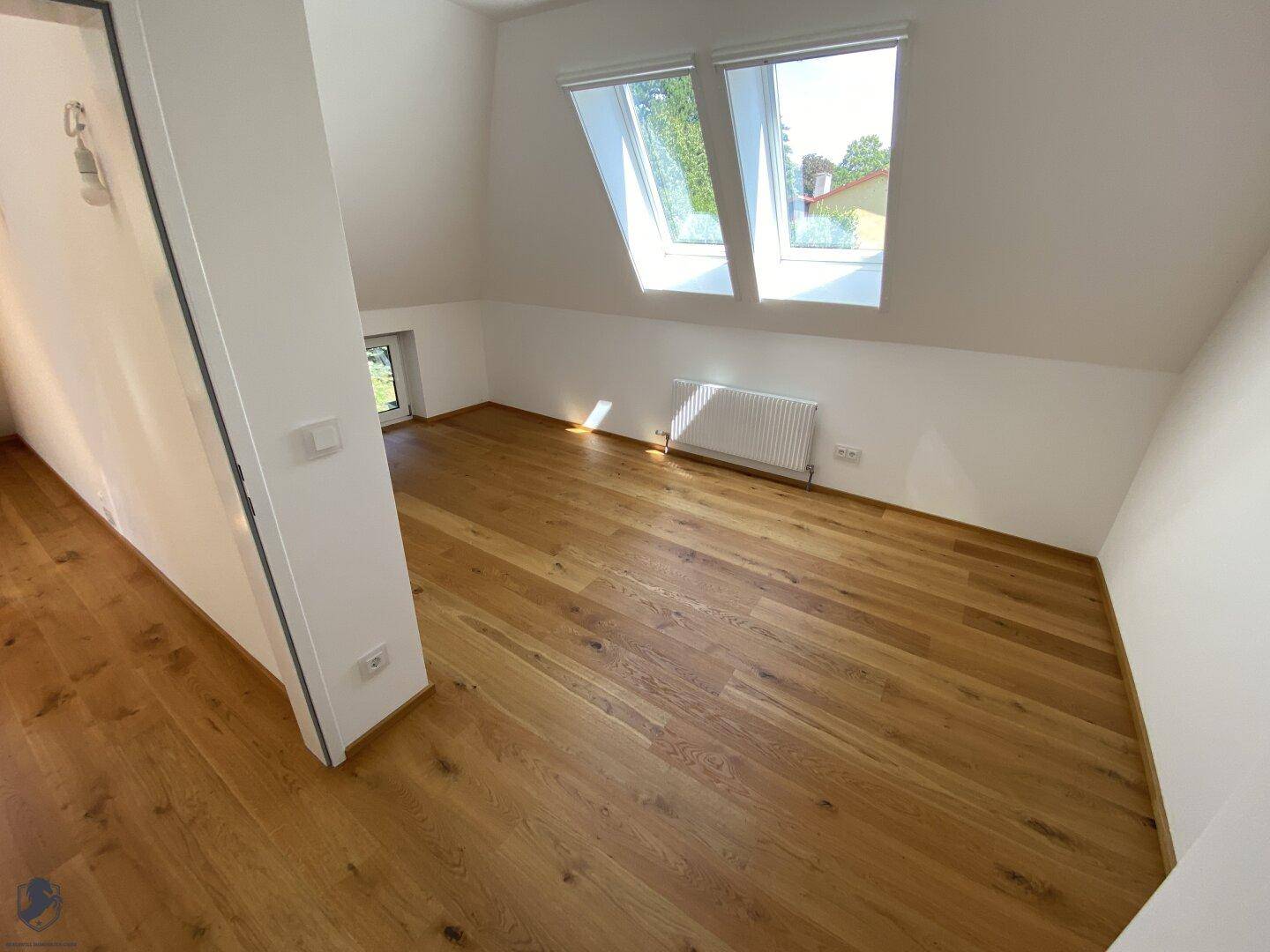 Helles Zimmer im Dachgeschoss mit Holzboden, Dachfenstern und Blick nach draußen.