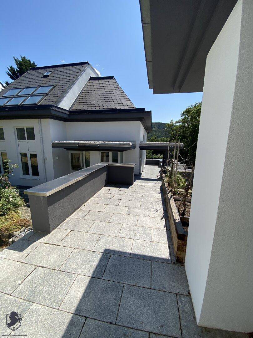 Gepflasterte Außenterrasse mit niedriger Mauer und Blick auf die umliegende Landschaft.