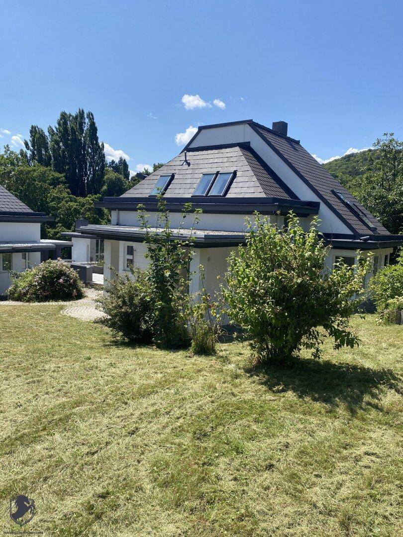 Seitenansicht eines modernen Hauses mit Schieferdach, Dachfenstern und weißer Fassade, umgeben von Rasen.