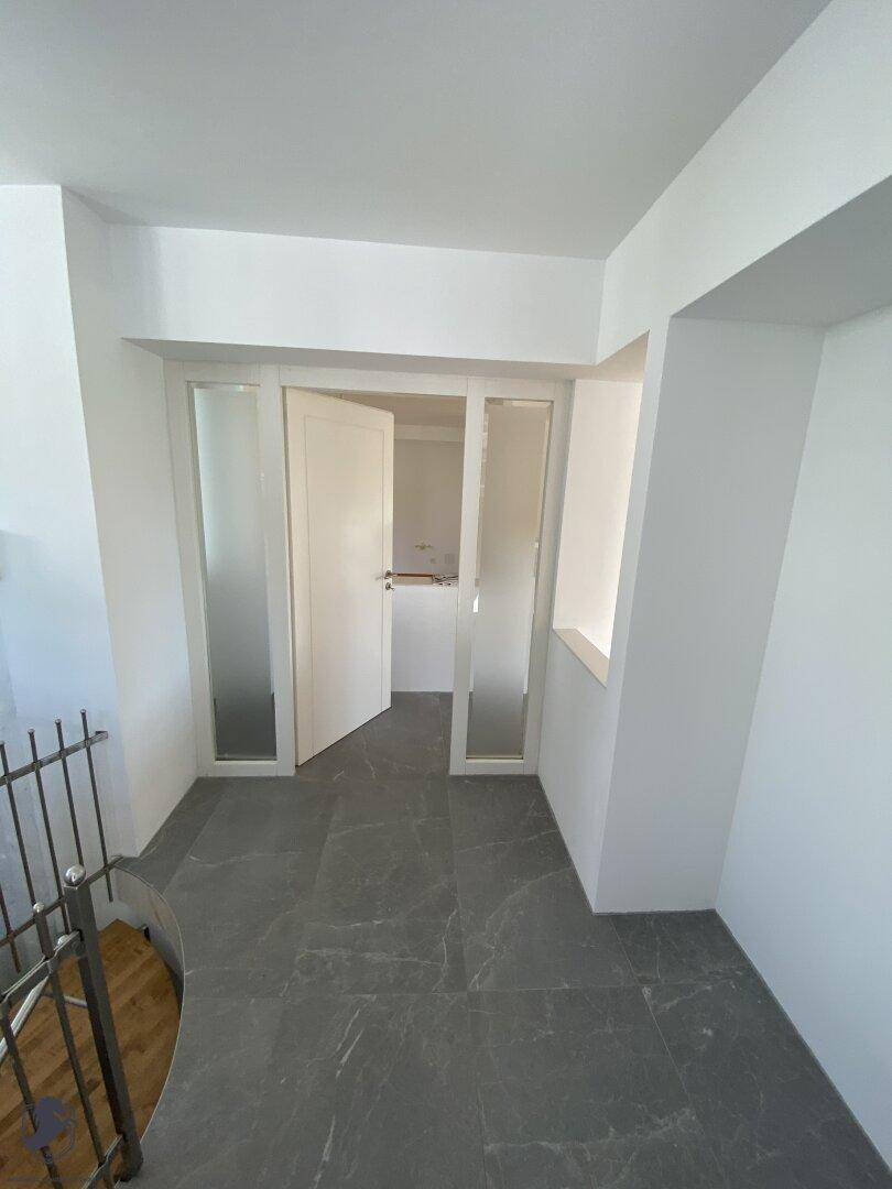 Eingangsbereich mit grauen Fliesen, weißer Tür und Blick auf die Treppe.