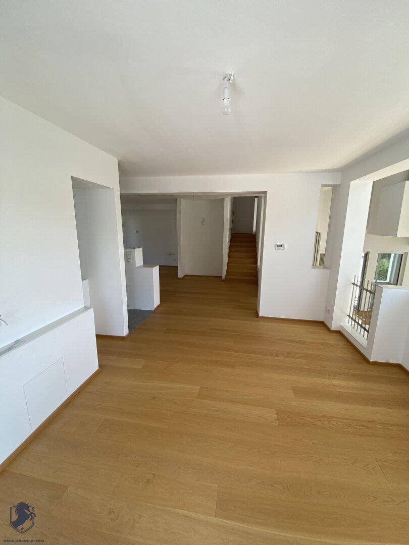 Offener Wohnbereich mit Holzboden, weißen Wänden und Blick auf den Flur.