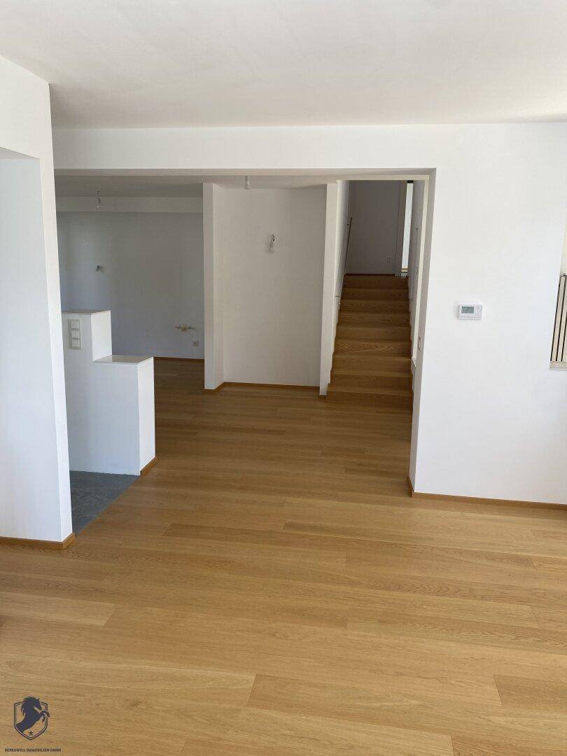 Geräumiger Wohnbereich mit Holzboden, weiß gestrichenen Wänden und Treppenzugang.