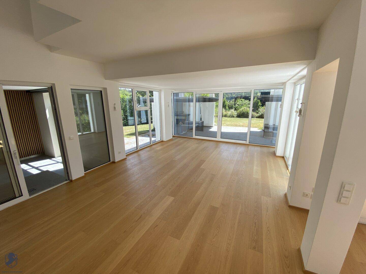 Heller Wohnbereich mit großen Glasfronten, Holzboden und Zugang zum Garten.