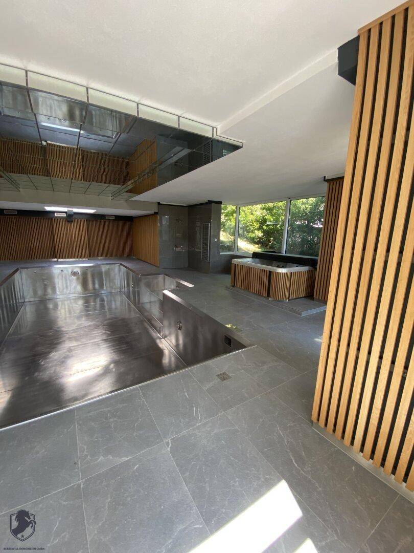 Moderner Innenpoolbereich mit Holzverkleidung und großen Fenstern, die viel Licht hereinlassen.
