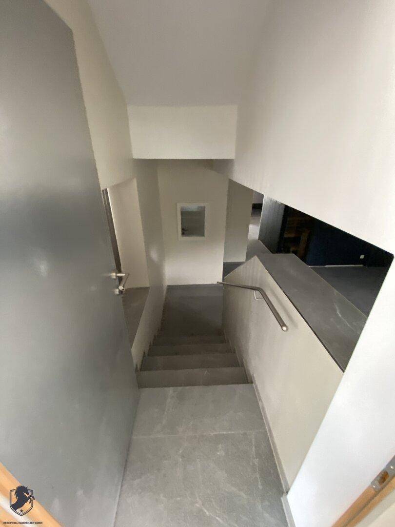 Modernes Treppenhaus mit grauen Fliesen, Geländer und Blick auf die untere Etage.