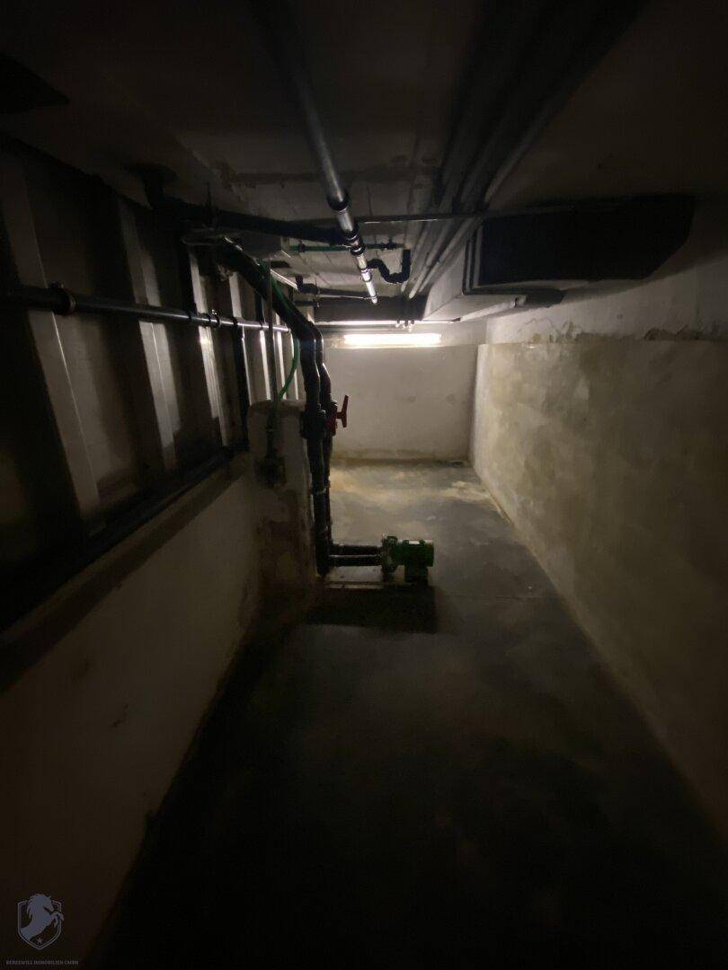 Dunkler Kellerraum mit Rohren an der Decke und begrenzter Beleuchtung.