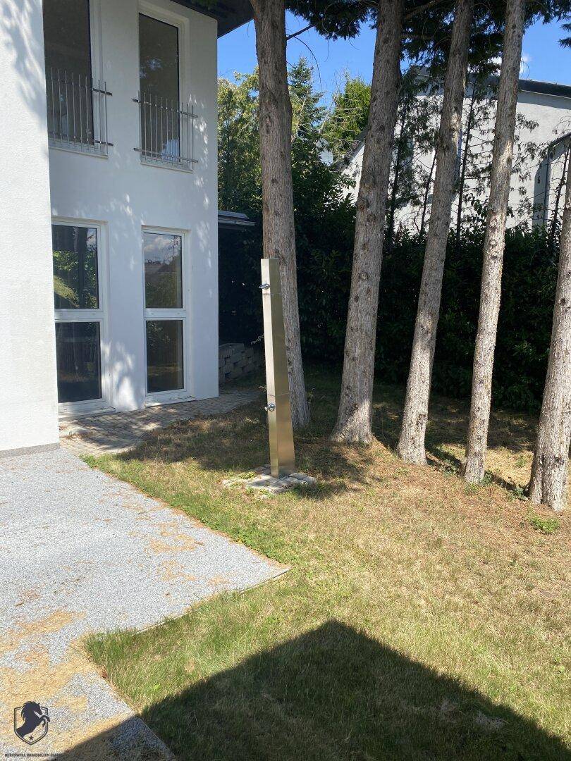 Gepflegter Gartenbereich mit Rasen, Bäumen und einer modernen Außendusche.