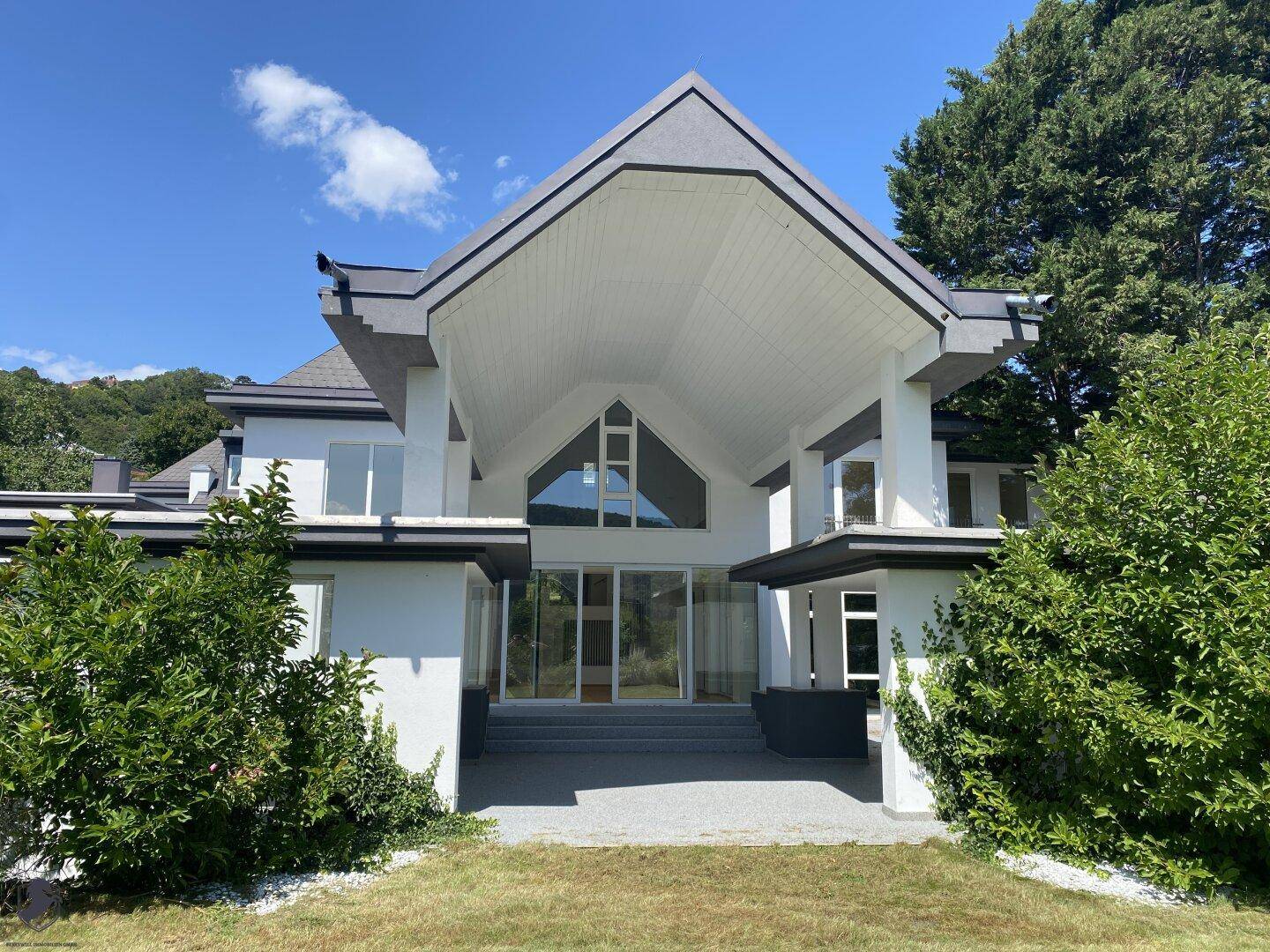 Moderne Hausfassade mit markantem Giebeleingang, großen Fenstern und gepflegtem Vorgarten.