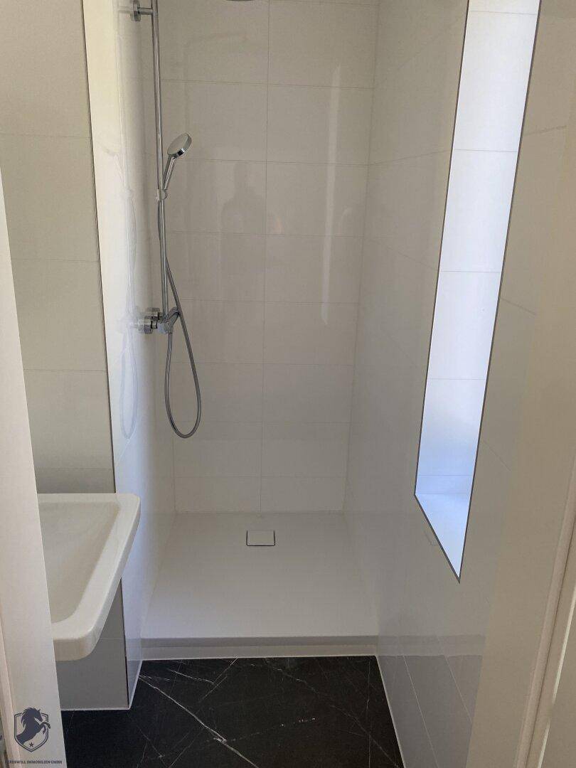 Moderne begehbare Dusche mit weißen Fliesen und dunklem Marmorboden, minimalistisch und hell.