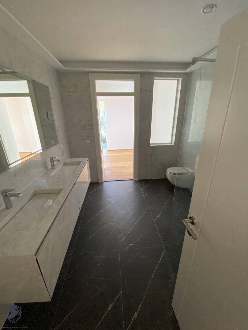 Elegantes Badezimmer mit Doppelwaschbecken, dunklem Fliesenboden und modernen Armaturen.