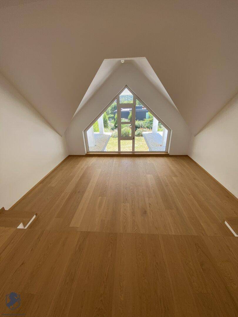 Helles Dachzimmer mit Holzboden und großem dreieckigem Fenster mit Blick auf den Garten.