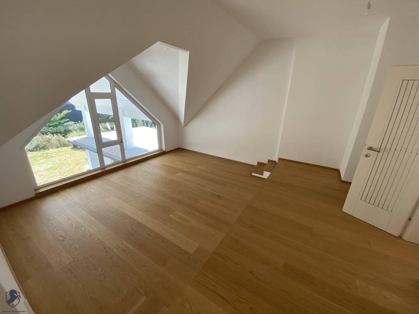 Geräumiges Dachzimmer mit Holzboden und schrägem Fenster, das viel Tageslicht hereinlässt.