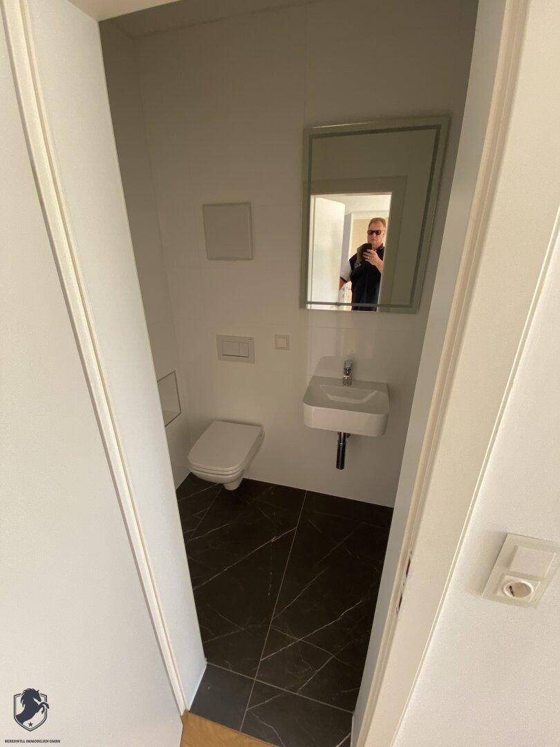 Kleines Gäste-WC mit modernem Waschbecken, Spiegel und dunklem Fliesenboden.