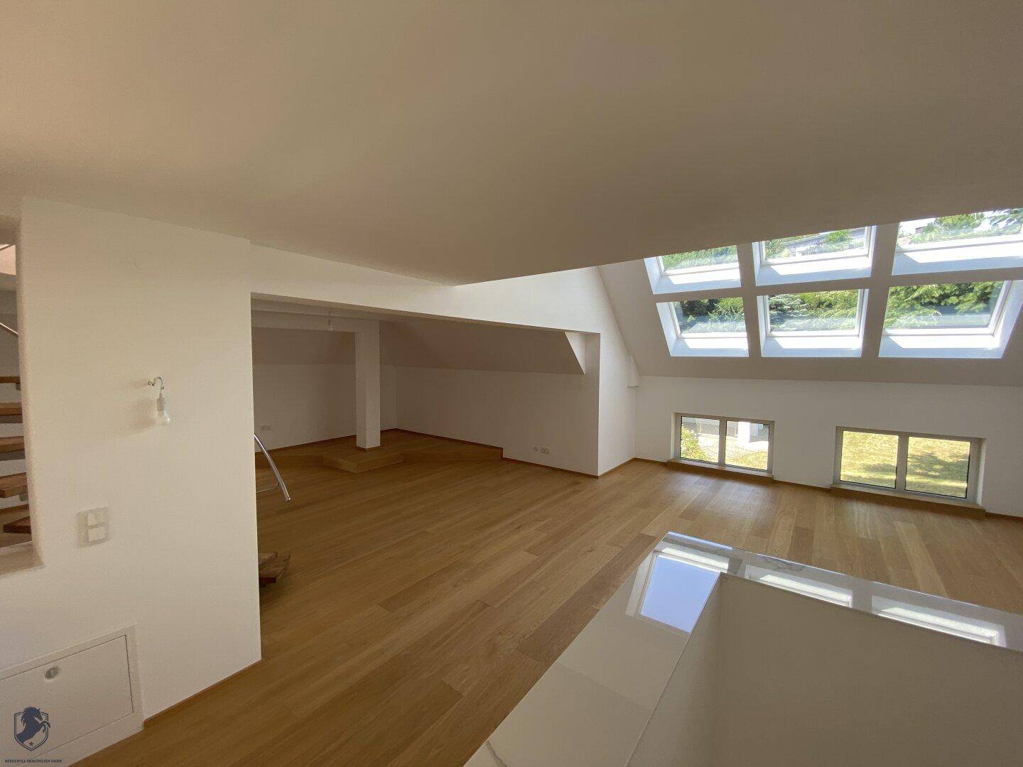 Heller und geräumiger Dachbodenbereich mit Holzboden und vielen Fenstern für natürliches Licht.