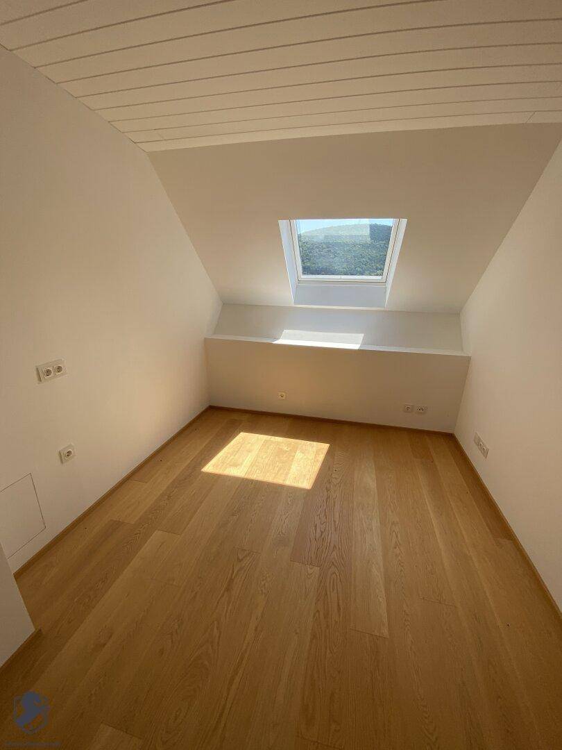 Kleines, helles Zimmer mit Holzboden und einem Dachfenster, ideal als Kinder- oder Arbeitszimmer.
