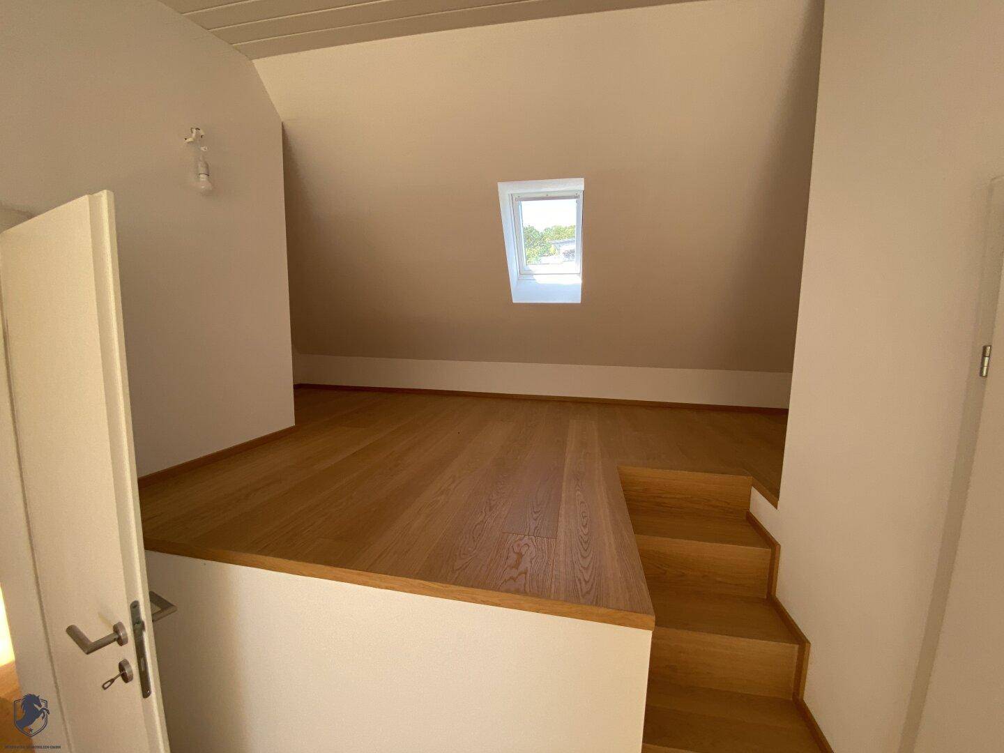 Helles Zimmer im Dachgeschoss mit Holzboden und einer erhöhten Plattform.