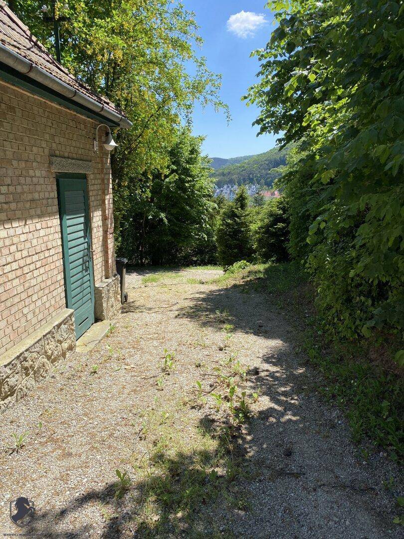 Schotterweg neben einem Backsteingebäude, umgeben von Bäumen mit Blick auf die Landschaft.