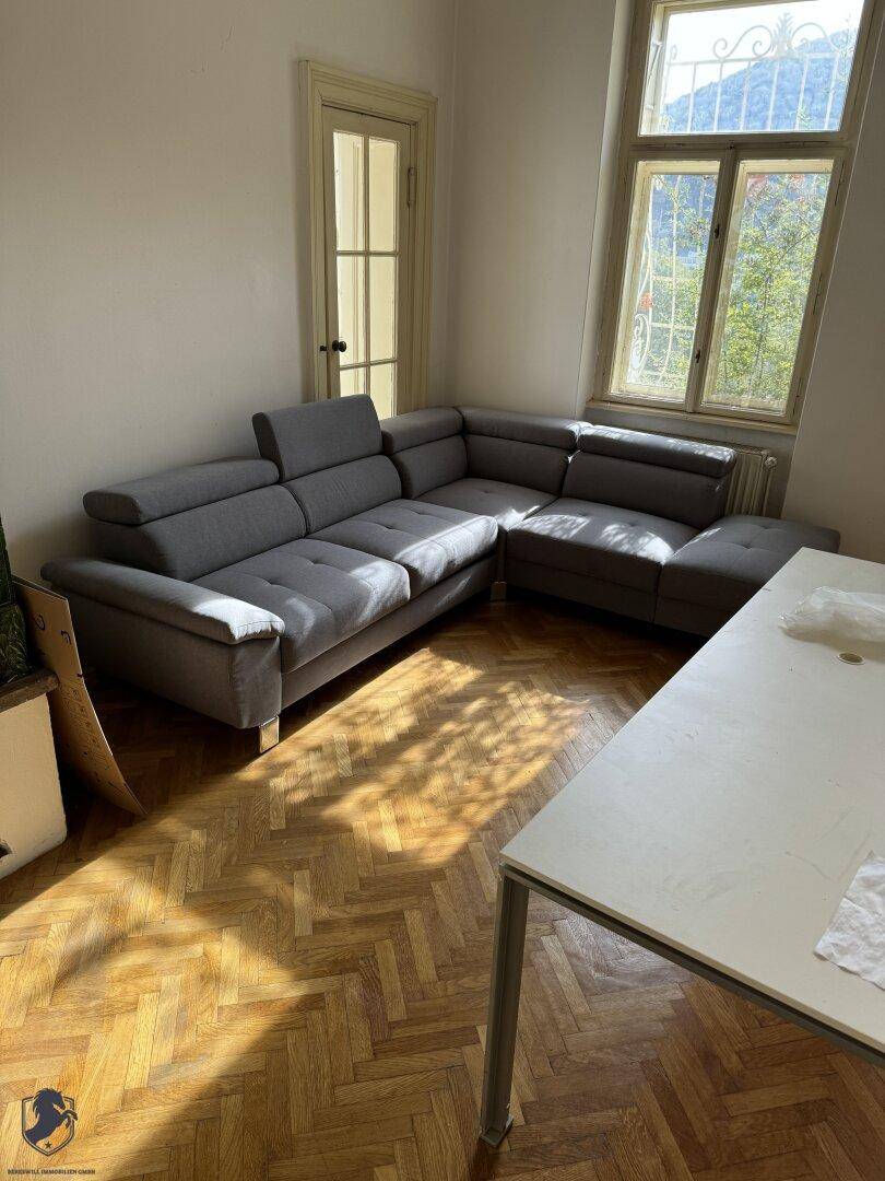 Helles Wohnzimmer mit Fischgrätparkett, modernem Ecksofa und großem Fenster.