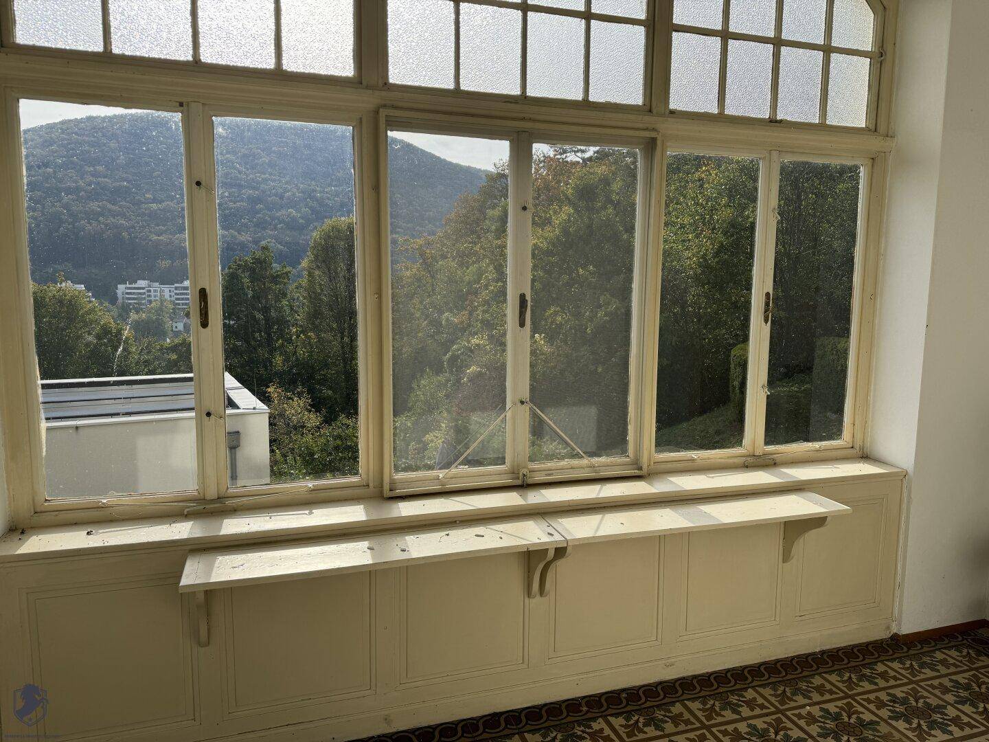 Heller Wintergarten mit großen Fenstern, die einen weiten Blick auf die grüne Umgebung bieten.