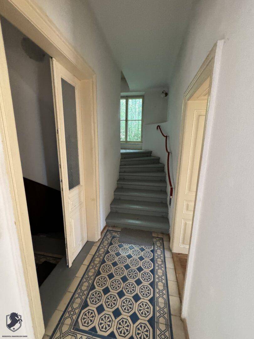 Flur mit gemusterten Fliesen und einer Treppe, die in die oberen Stockwerke führt.