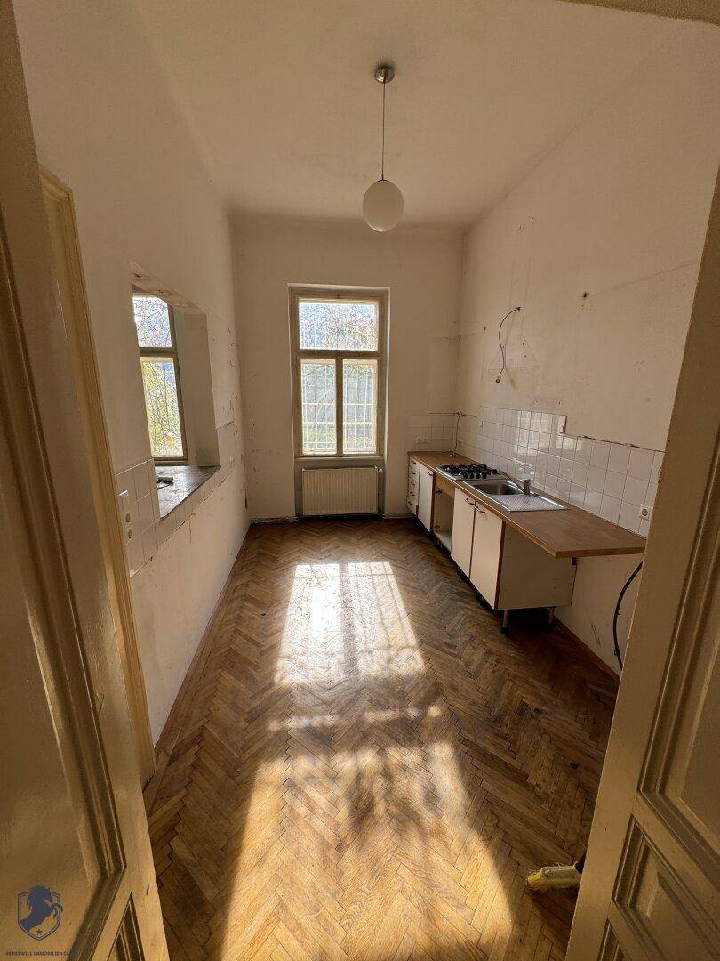Küche mit Fischgrätparkett, einfachen Unterschränken und einem Fenster mit viel Tageslicht.