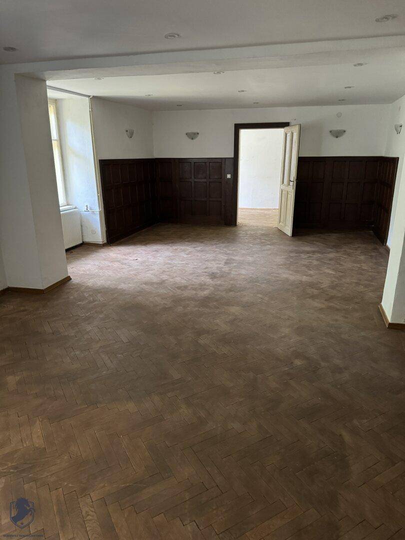 Geräumiger Raum mit dunklem Fischgrätparkett und Holzvertäfelung an den Wänden.