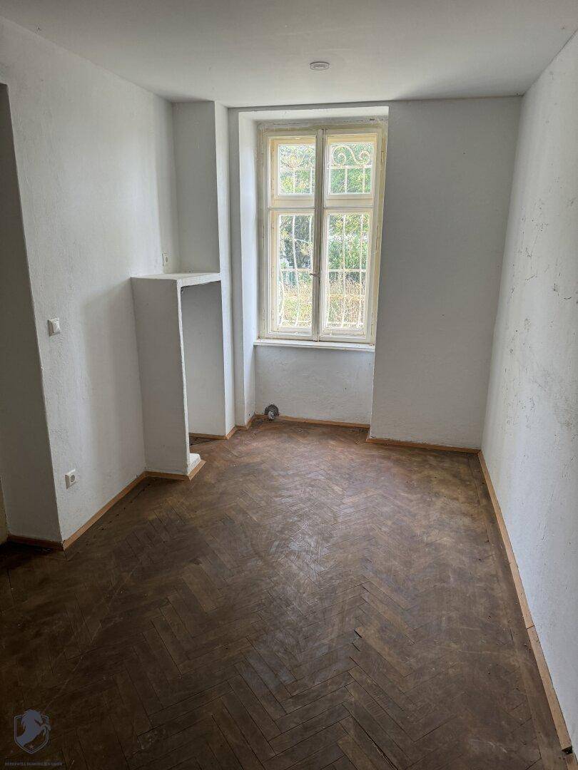 Helles Zimmer mit dunklem Fischgrätparkett und einem Fenster, das viel Tageslicht hereinlässt.
