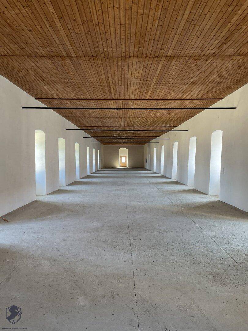 Langer, leerer Raum mit Holzbalkendecke und vielen Fenstern, bereit für den Ausbau.