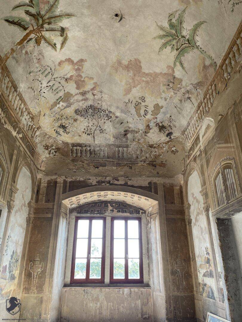 Historischer Raum mit aufwendigen Deckenmalereien und Fenstern, die eine Renovierung benötigen.
