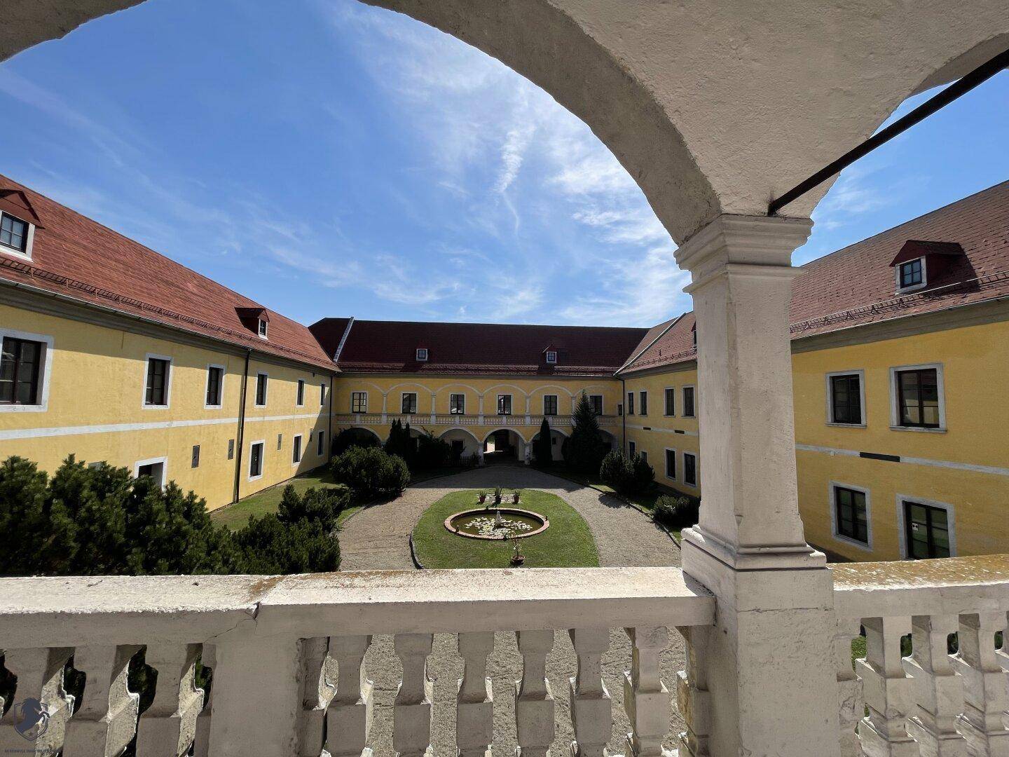 Heller Arkadengang mit Blick durch einen Bogen auf den weitläufigen Schlosshof.