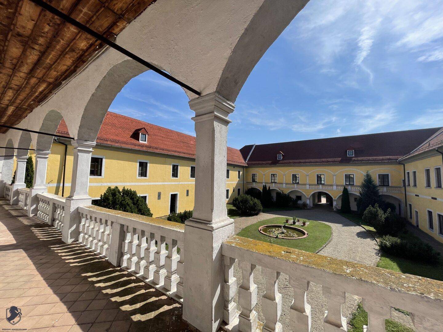 Überdachter Arkadengang mit Balustrade und Blick auf den sonnigen Innenhof des historischen Schlosses.