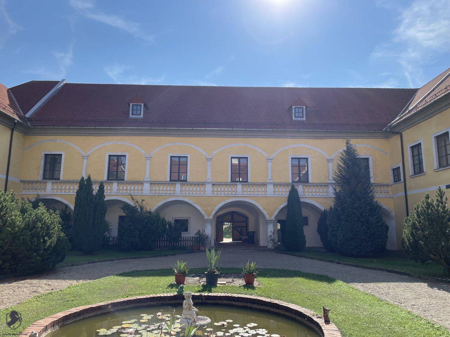 Symmetrischer Innenhof des Schlosses mit zentralem Brunnen und gepflegten Grünflächen unter blauem Himmel.