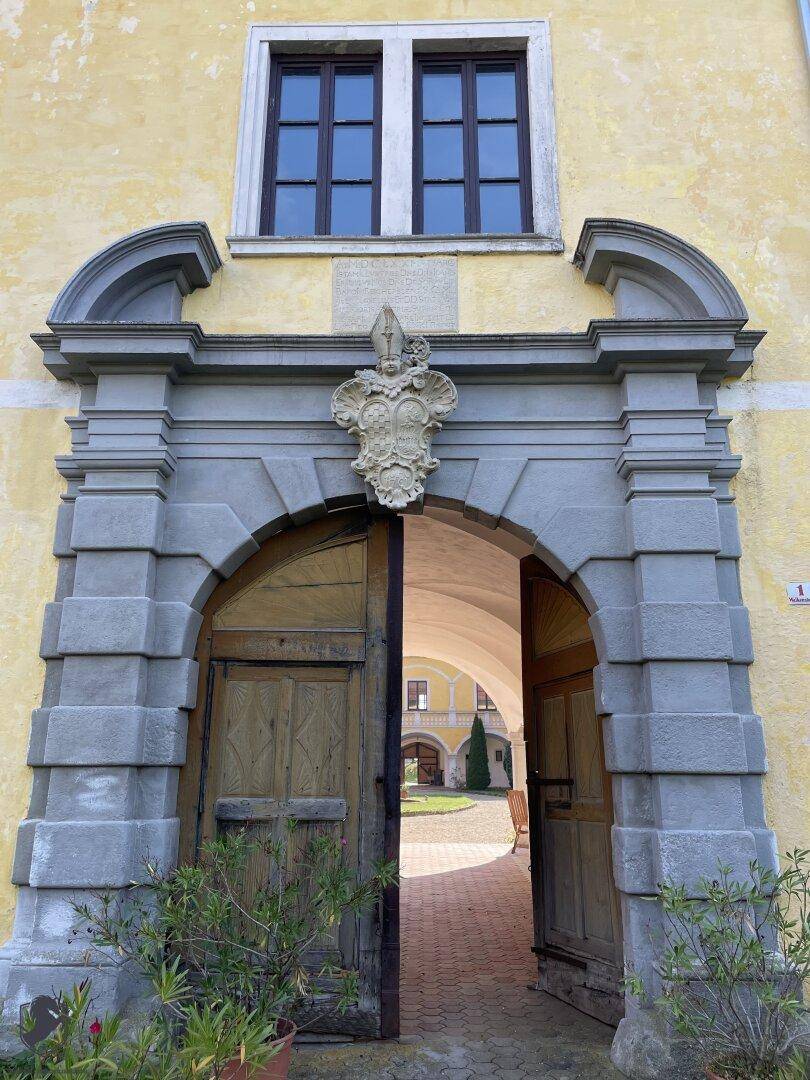 Prunkvolles historisches Eingangsportal mit Wappen und massiven Holztüren, die zum Innenhof führen.