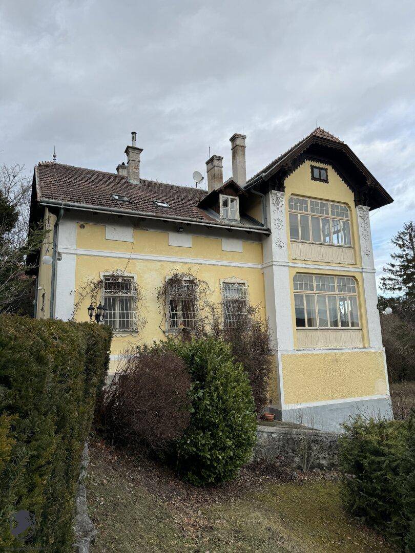 Historische Villa mit gelber Fassade, vielen Fenstern und traditionellem Dach unter bewölktem Himmel.