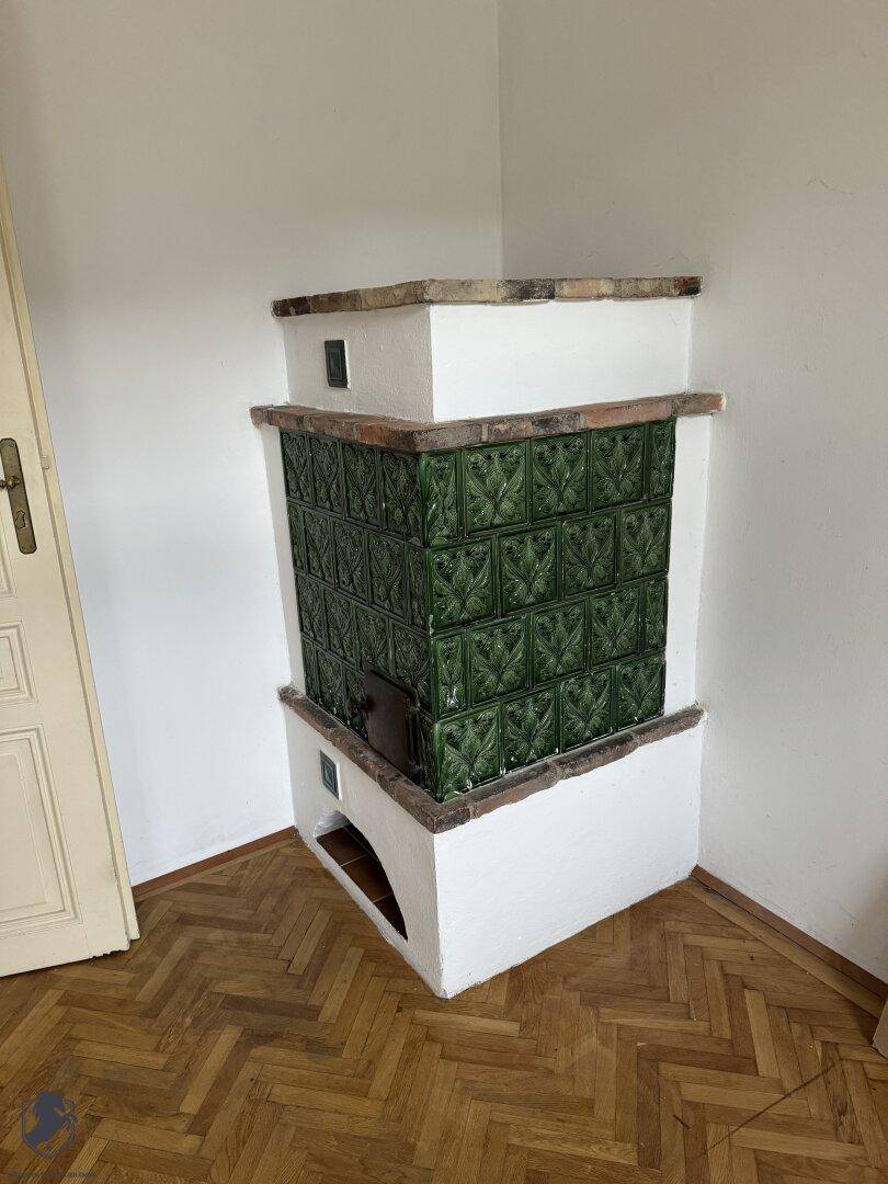 Zimmer mit Fischgrätparkett und einem traditionellen grünen Kachelofen als Heizelement.