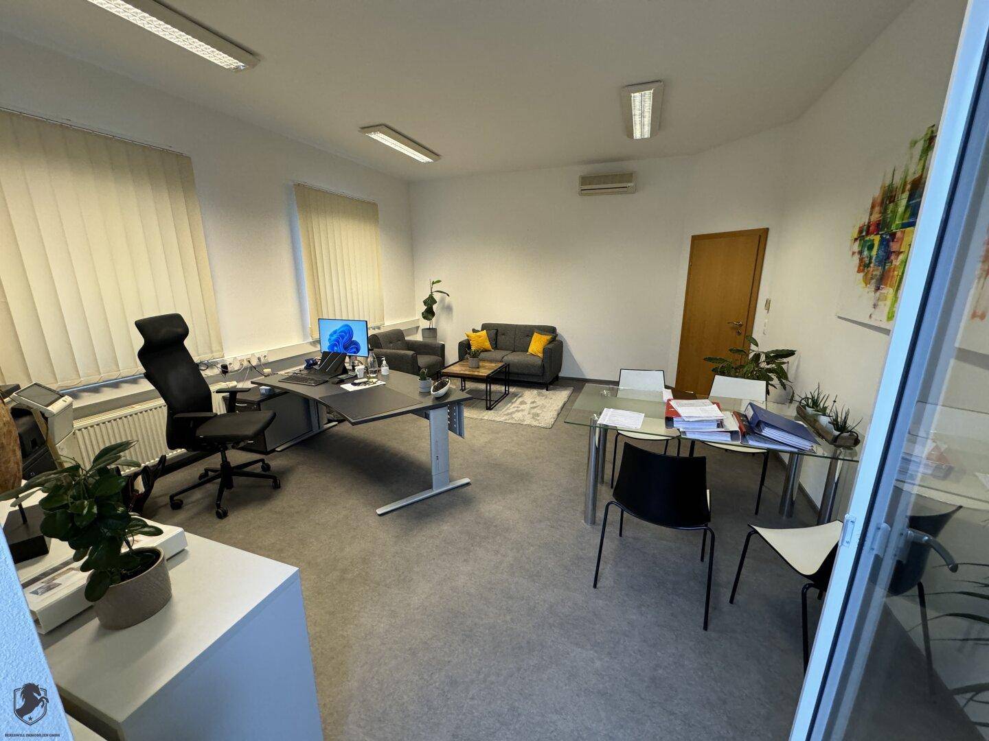Modernes Büro mit Schreibtisch, bequemer Sitzecke und einem Besprechungstisch, hell und funktional eingerichtet.