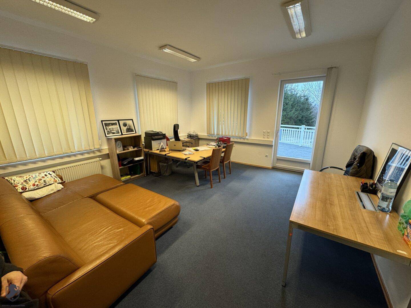 Geräumiges Büro mit einem großen braunen Ledersofa, einem Schreibtisch und Teppichboden.