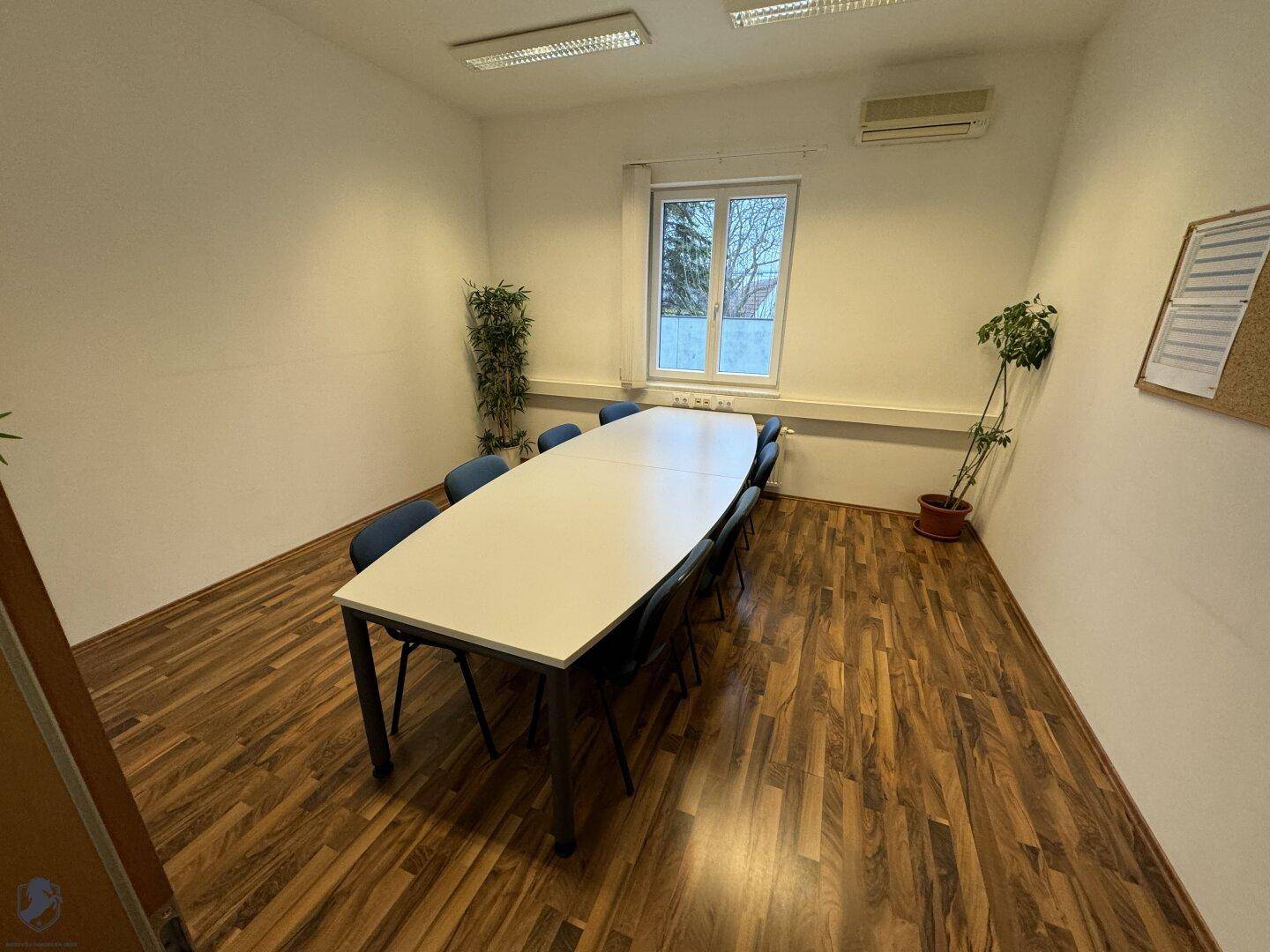 Konferenzraum mit einem langen Besprechungstisch, Stühlen und einem pflegeleichten Laminatboden.