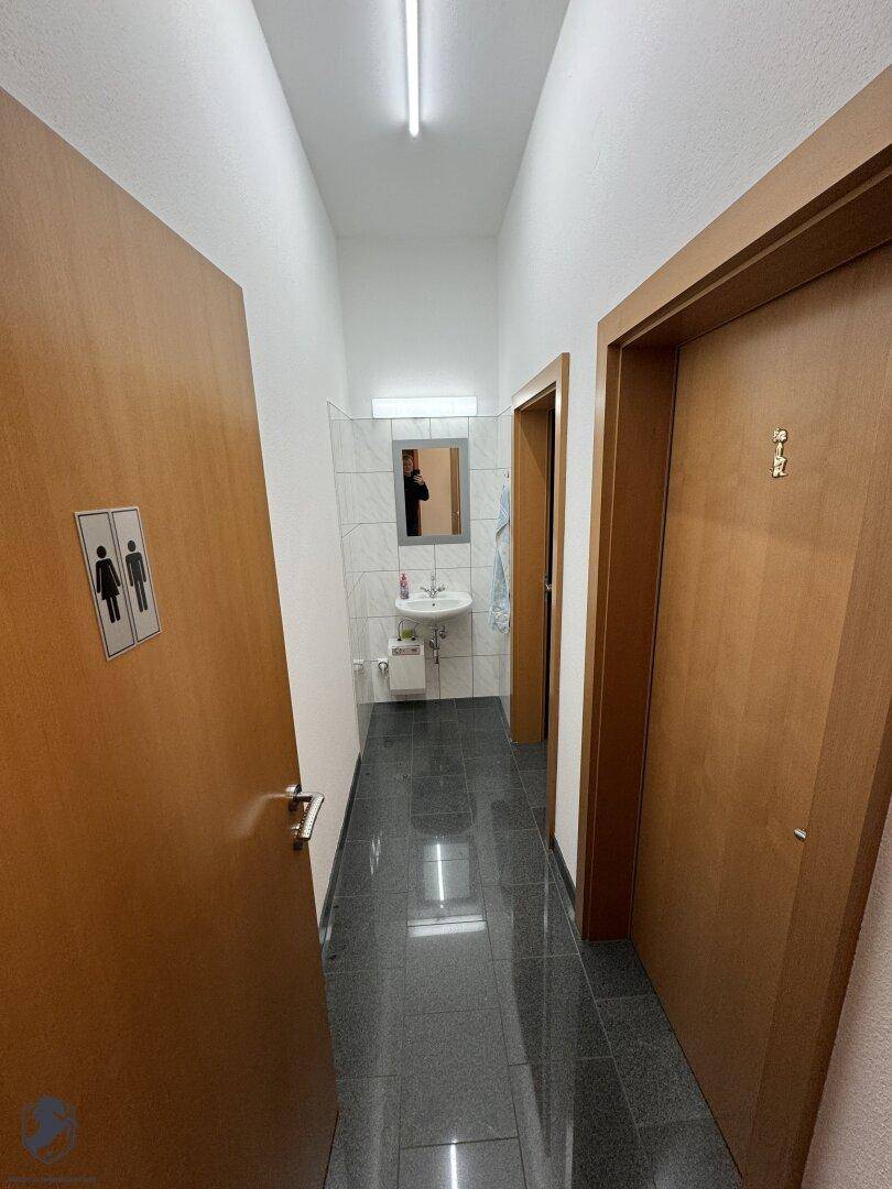 Heller Badezimmerflur mit dunklem Fliesenboden, der zu einem Waschbeckenbereich führt.
