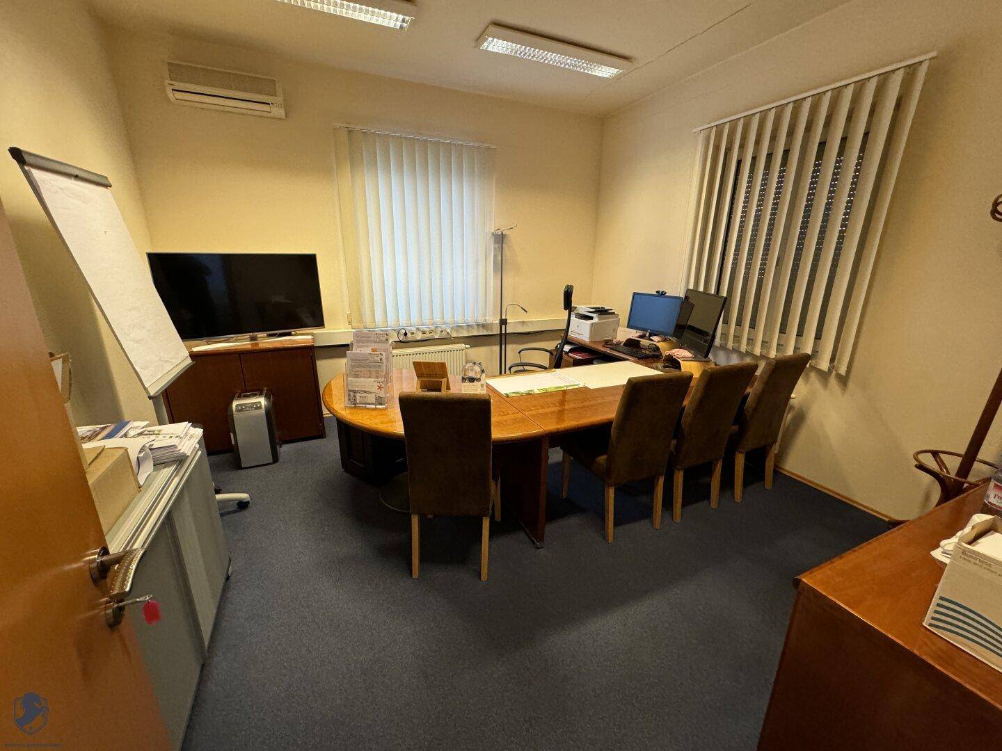 Klassisch eingerichtetes Büro mit einem großen ovalen Schreibtisch, bequemen Stühlen und Teppichboden.