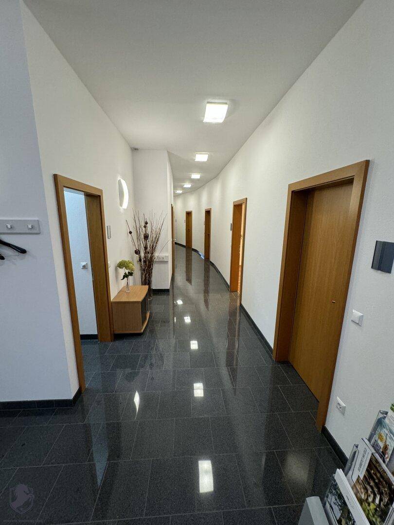 Langer, sauberer Flur mit dunklem Fliesenboden und mehreren Holztüren, die zu den verschiedenen Räumen führen.