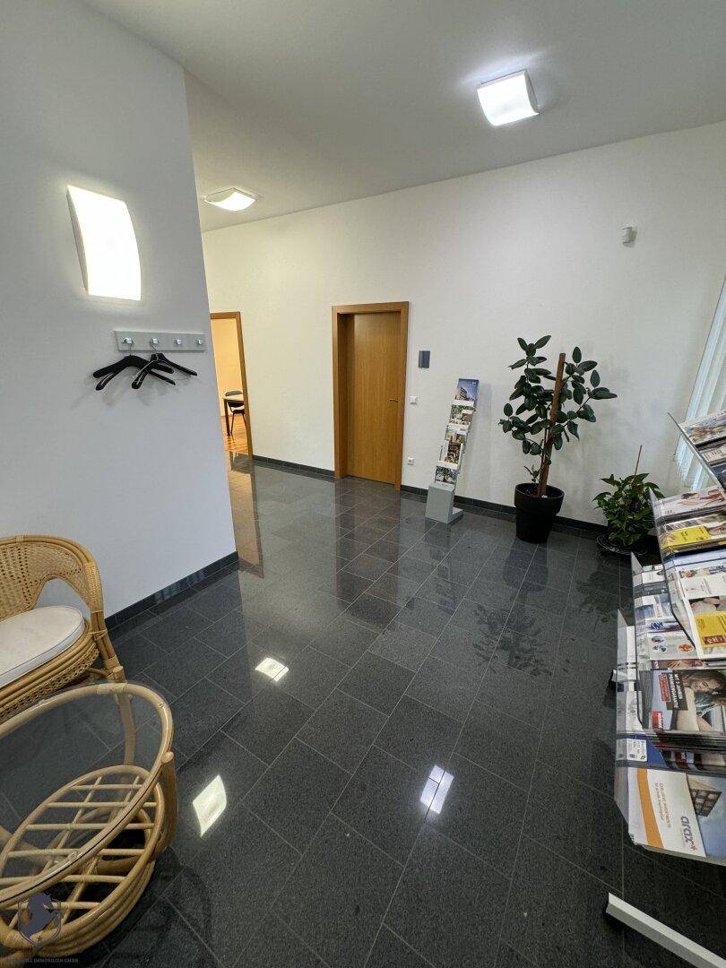 Empfangsbereich oder Wartezimmer mit dunklem Fliesenboden, einer Sitzgelegenheit und dekorativen Pflanzen.