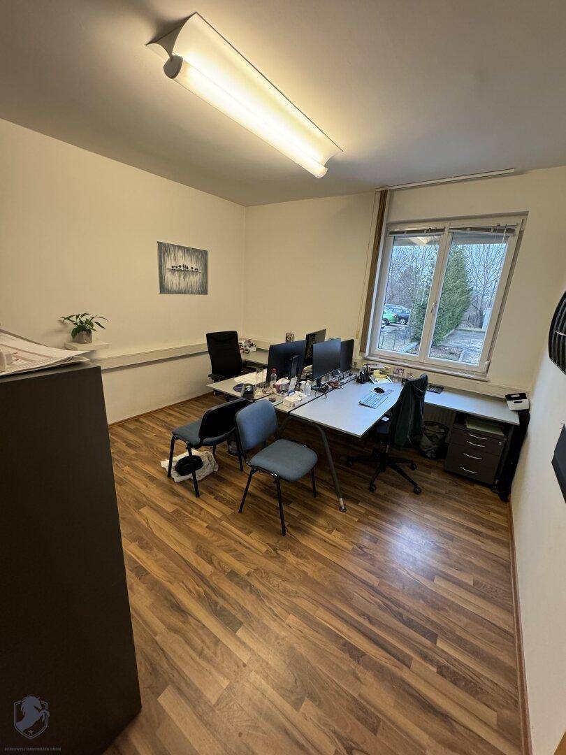 Büro mit mehreren Arbeitsplätzen, Laminatboden und einem großen Fenster, das viel Licht spendet.